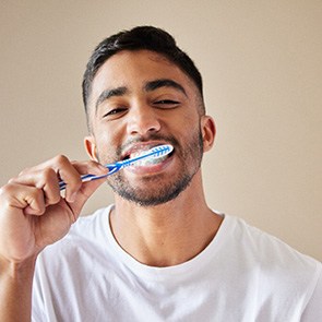 A young man brushing his teeth in front of a bathroom mirror