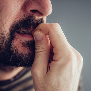A closeup of a bearded man biting his fingernails