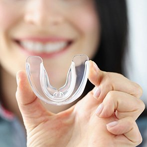 A smiling woman holding up a transparent plastic mouthguard