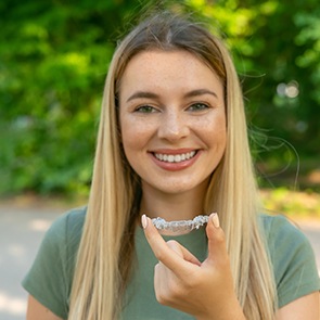 A happy, smiling woman holding an Invisalign tray in front of her