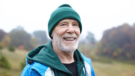 Senior man with beanie standing in middle of field smiling