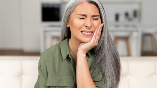 an older woman holding her cheek due to tooth pain