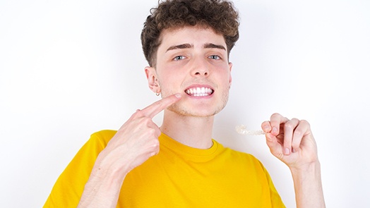 Teenage boy in yellow shirt holding Invisalign and pointing to smile